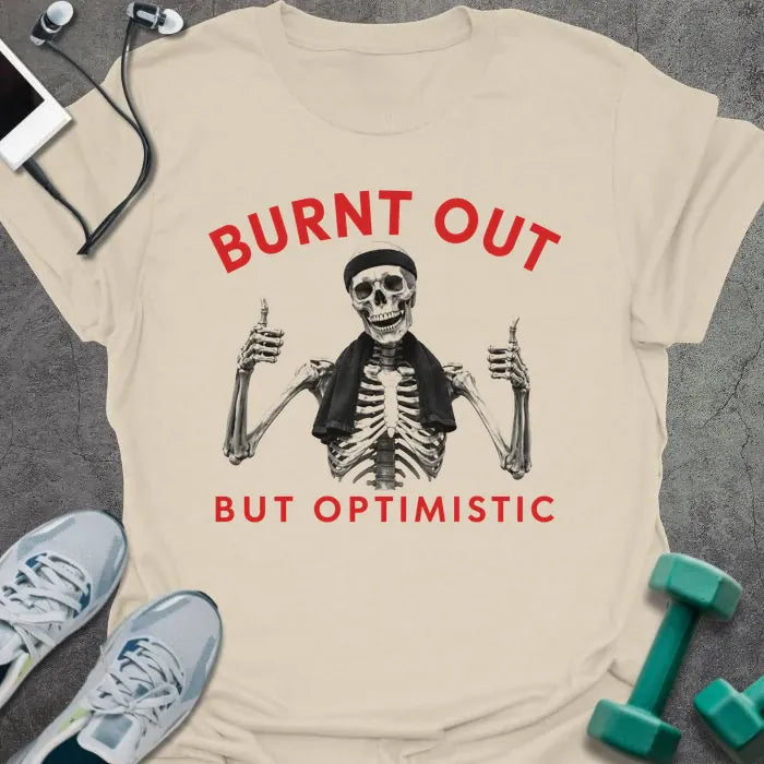 Natural t-shirt printed with "BURNT OUT but OPTIMISTIC" in red and black, with skeleton with dumbbells