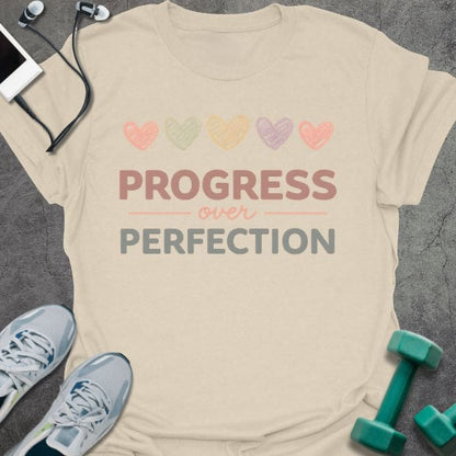 Cream t-shirt printed with "PROGRESS over PERFECTION" in multi-color, with five hearts in pastel colors