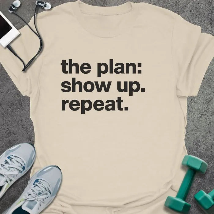 Natural t-shirt printed with "the plan: show up. repeat." in black lettering