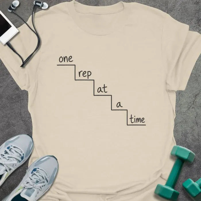 Natural t-shirt printed with "one rep at a time" in black line art, with staircase graphic