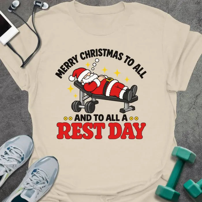 Natural t-shirt printed with "MERRY CHRISTMAS TO ALL AND TO ALL A REST DAY" in black and red, with Santa asleep on a weight bench