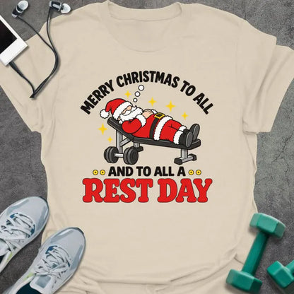 Natural t-shirt printed with "MERRY CHRISTMAS TO ALL AND TO ALL A REST DAY" in black and red, with Santa asleep on a weight bench