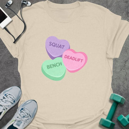 Cream t-shirt printed with "Squat Bench Deadlift" in purple, green, pink, with three conversation candy hearts in purple, green, and pink
