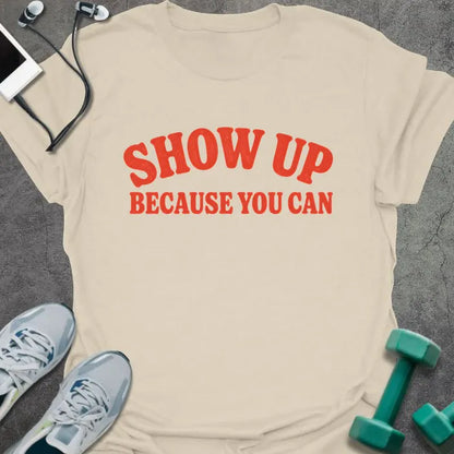 Natural t-shirt printed with "SHOW UP BECAUSE YOU CAN" in red bold text