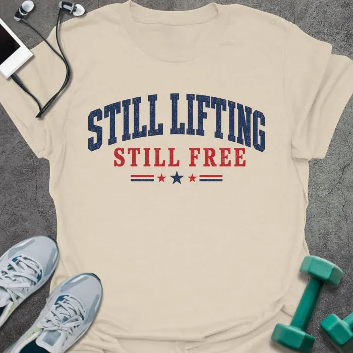 Cream t-shirt printed with "Still Lifting Still Free" in blue and red, with stars