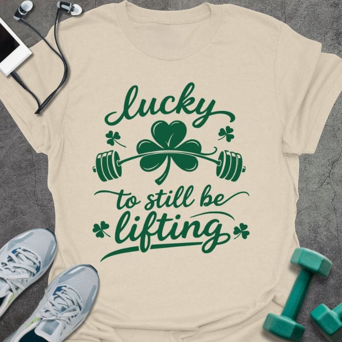 Cream t-shirt printed with "lucky to still be lifting" in green, with clover, shamrock and barbell
