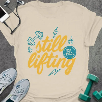 Cream t-shirt printed with "still lifting EST. 1960s" in yellow and cyan, with lightning bolts and dumbbell graphics