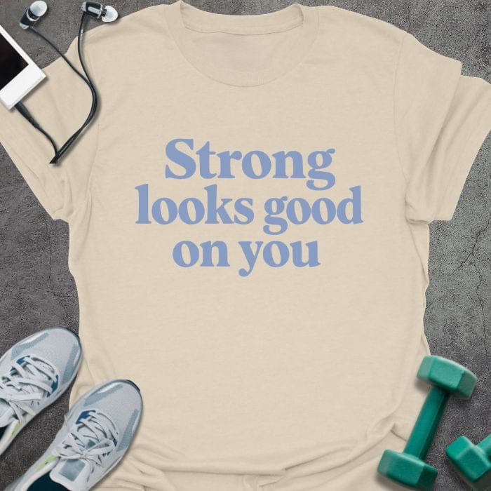Cream t-shirt printed with "Strong looks good on you" in blue
