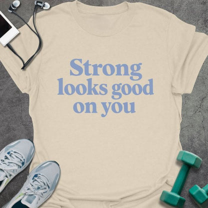 Cream t-shirt printed with "Strong looks good on you" in blue