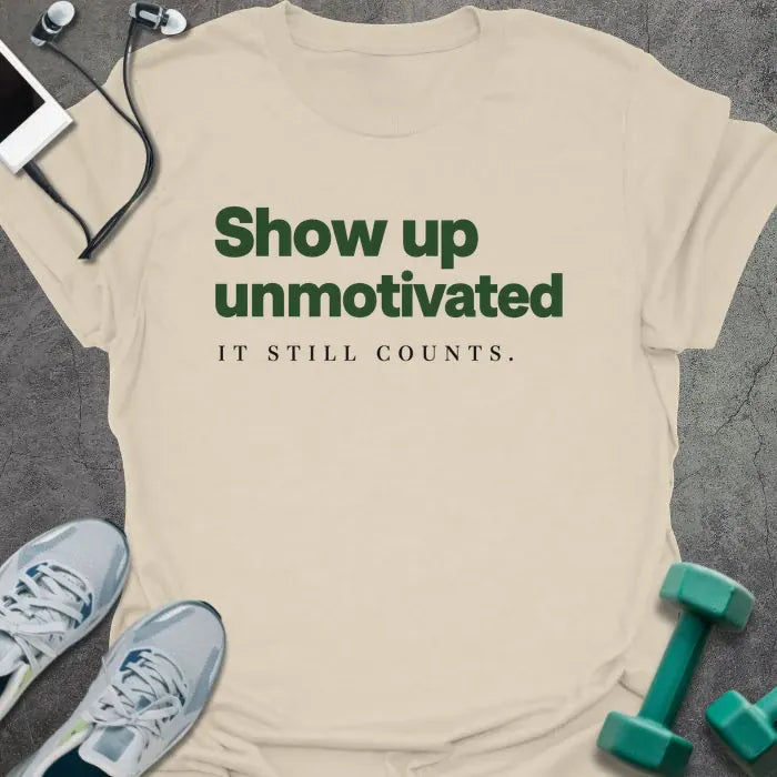 Natural t-shirt printed with "Show up unmotivated IT STILL COUNTS." in green and black