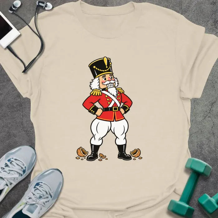 Natural t-shirt printed with a vintage nutcracker soldier with strong legs, hands on hips, standing over cracked nutshells