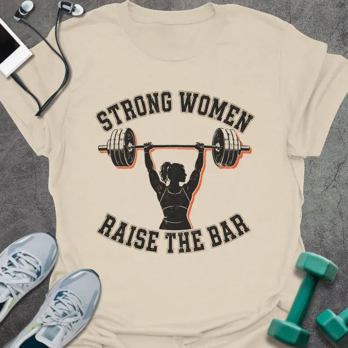 Natural t-shirt printed with "STRONG WOMEN RAISE THE BAR" in black lettering, with a silhouette of a woman weightlifter raising a barbell overhead