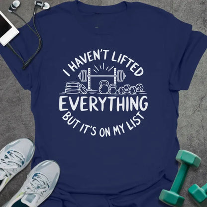 Navy t-shirt printed with "I HAVEN'T LIFTED EVERYTHING BUT IT'S ON MY LIST" in white, with a barbell, weight plates, kettlebells and dumbbells