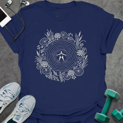 Navy t-shirt printed with cream line art of a woman floating on her back in a rippling pond, ringed by water lilies, lily pads, cattails and koi
