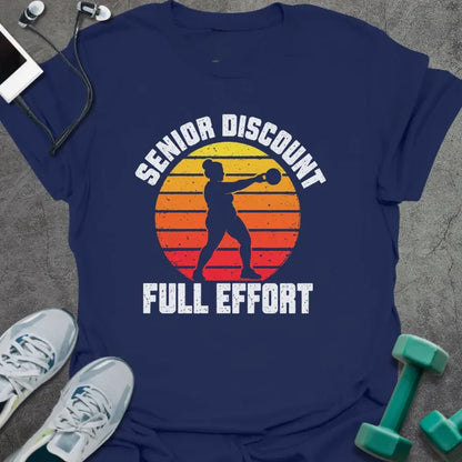 Navy t-shirt printed with "SENIOR DISCOUNT, FULL EFFORT" in white, with a woman swinging a kettlebell against a retro yellow, orange and red sunset