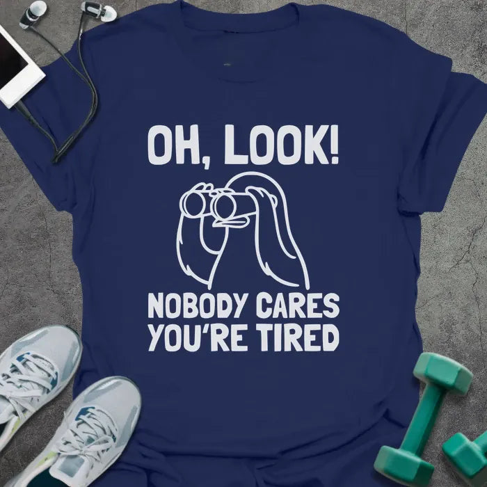 Navy t-shirt printed with "Oh, Look! Nobody Cares You're Tired", with an illustration of a person with binoculars