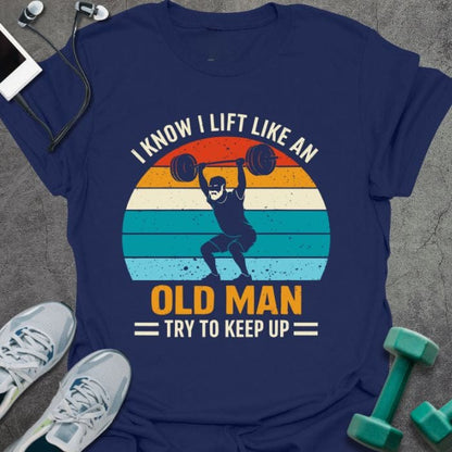 Navy t-shirt printed with "I Know I Lift Like an Old Man Try to Keep Up" in orange, white, green, light blue, with a person lifting and rainbow sunset background