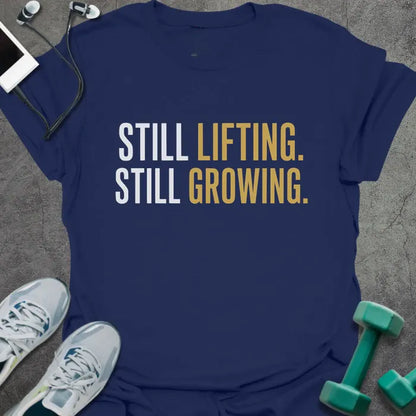 Navy t-shirt printed with "Still Lifting. Still Growing." in white and gold