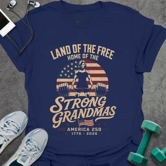Navy t-shirt printed with "Land of the Free Home of the Strong Grandmas America 250 1776 - 2026" in tan and white, with a weightlifting woman silhouette and American flag