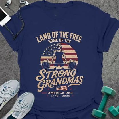Navy t-shirt printed with "Land of the Free Home of the Strong Grandmas America 250 1776 - 2026" in tan and white, with a weightlifting woman silhouette and American flag