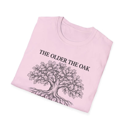 Folded light pink t-shirt printed with "THE OLDER THE OAK, THE STRONGER IT STANDS" in black, with a drawing of an oak tree and its roots