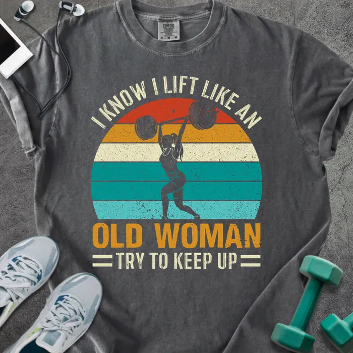 Pepper t-shirt printed with "I Know I Lift Like an Old Woman Try to Keep Up" in orange and multicolor, with a lifting silhouette and rainbow sunset