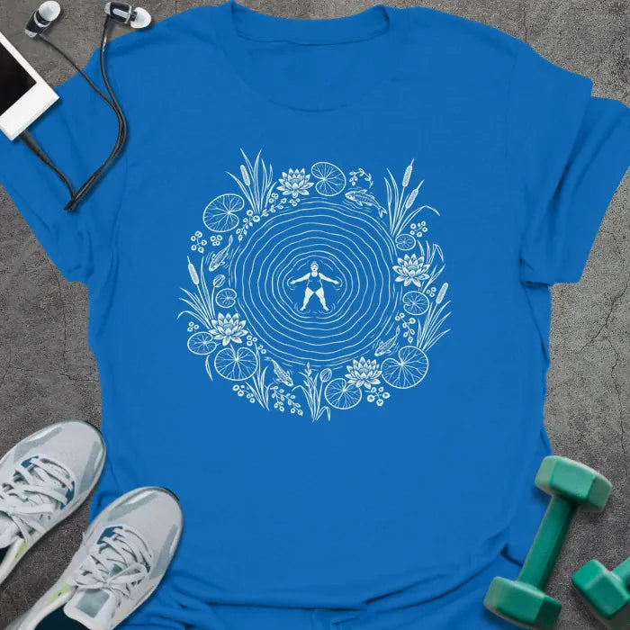 Royal blue t-shirt printed with cream line art of a woman floating on her back in a rippling pond, ringed by water lilies, lily pads, cattails and koi