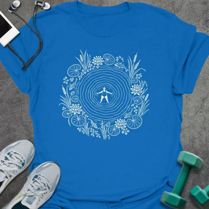 Royal blue t-shirt printed with cream line art of a woman floating on her back in a rippling pond, ringed by water lilies, lily pads, cattails and koi