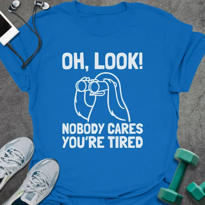 Royal blue t-shirt printed with "Oh, Look! Nobody Cares You're Tired", with an illustration of a person with binoculars