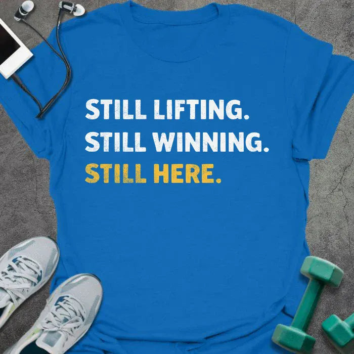 Royal blue t-shirt printed with "Still Lifting. Still Winning. Still Here." in white and yellow