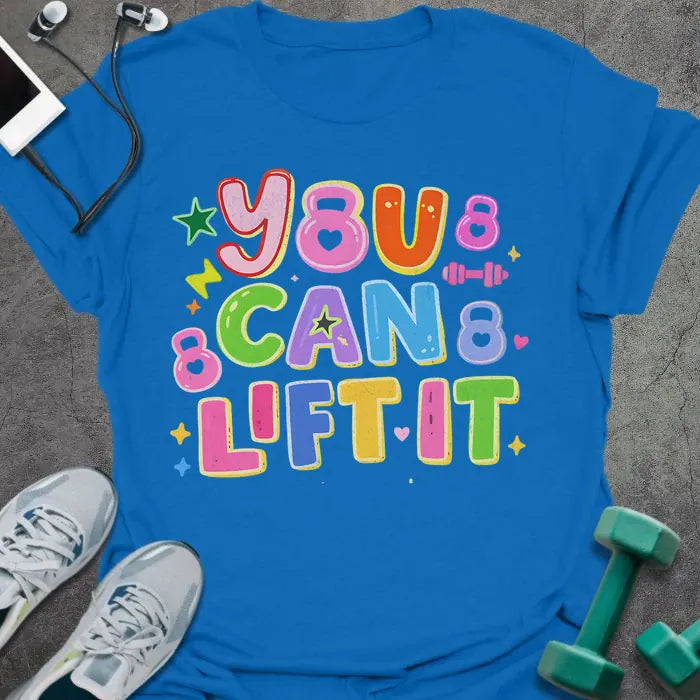 Royal blue t-shirt printed with "You Can Lift it" in pink, orange, green, purple, blue, yellow, with bubble letters, stars, sparkles, and small dumbbell doodles