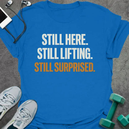 Royal blue t-shirt printed with "Still Here. Still Lifting. Still Surprised." in white and orange