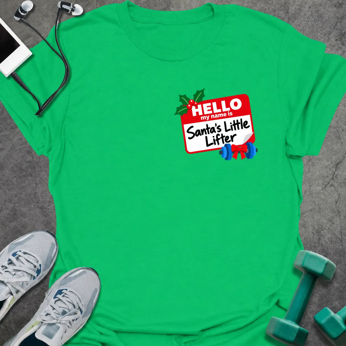 Irish green t-shirt printed with a small red name tag on the chest reading "HELLO my name is Santa's Little Lifter", with holly and a blue dumbbell tied with a red bow