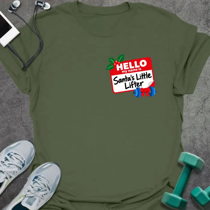 Military green t-shirt printed with a small red name tag on the chest reading "HELLO my name is Santa's Little Lifter", with holly and a blue dumbbell tied with a red bow