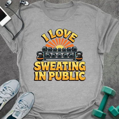 Sport grey t-shirt printed with "I LOVE SWEATING IN PUBLIC" in yellow and orange, with a dumbbell rack, kettlebells and a retro sunset