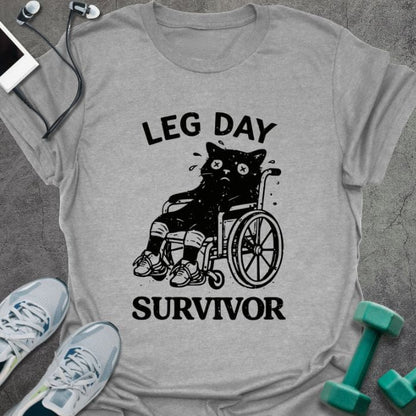 Sport grey t-shirt printed with "Leg Day Survivor", with a black cat with X eyes sitting in a wheelchair with bandaged legs