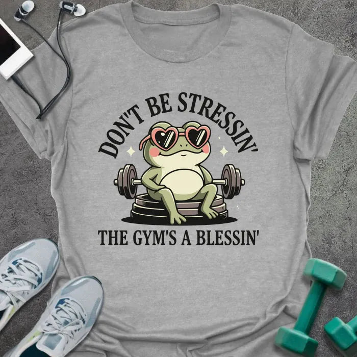 Sport grey t-shirt printed with "Don't Be Stressin' the Gym's a Blessin'" in red, with an illustration of a frog with heart-shaped sunglasses lifting dumbbells