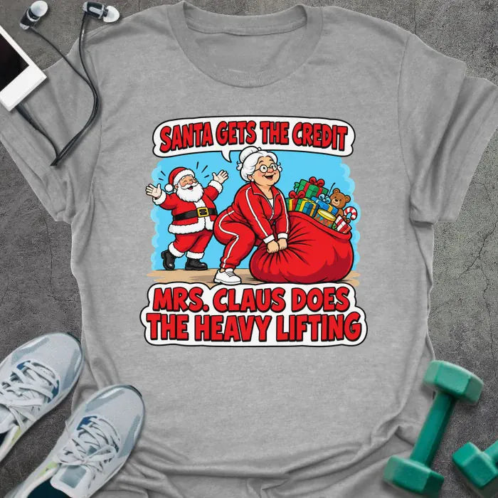 Sport grey t-shirt printed with "SANTA GETS THE CREDIT, MRS. CLAUS DOES THE HEAVY LIFTING" in red and white, with Mrs. Claus hauling a sack of gifts while Santa waves