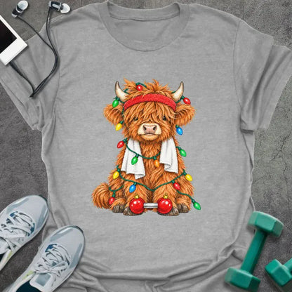 Sport grey t-shirt printed with a fluffy highland cow in a red headband and towel, tangled in Christmas lights beside a barbell with ornament plates
