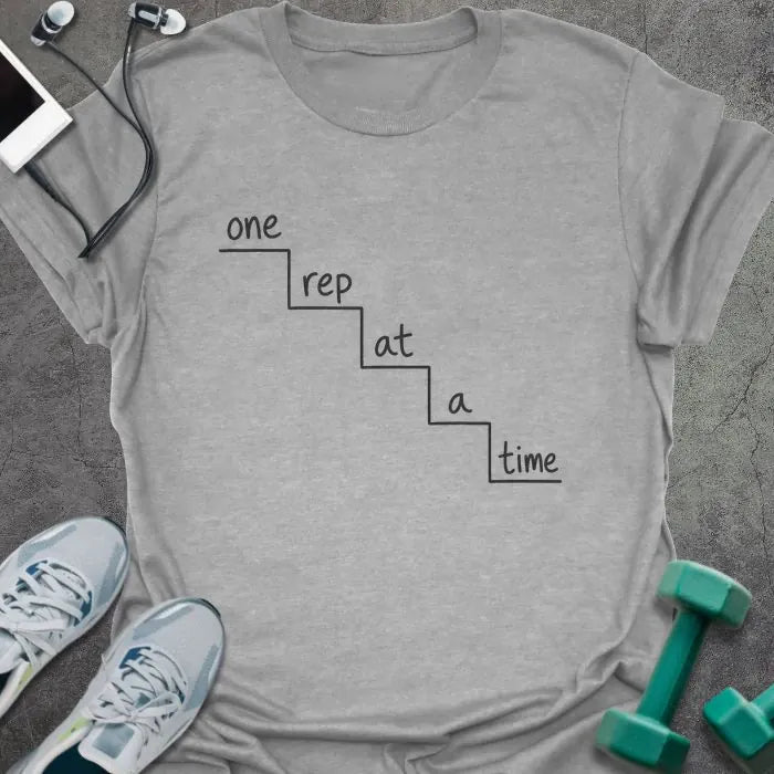 Sport grey t-shirt printed with "one rep at a time" in black line art, with staircase graphic