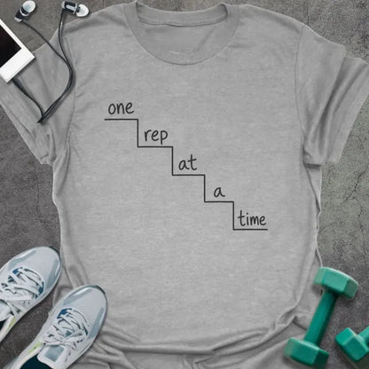 Sport grey t-shirt printed with "one rep at a time" in black line art, with staircase graphic