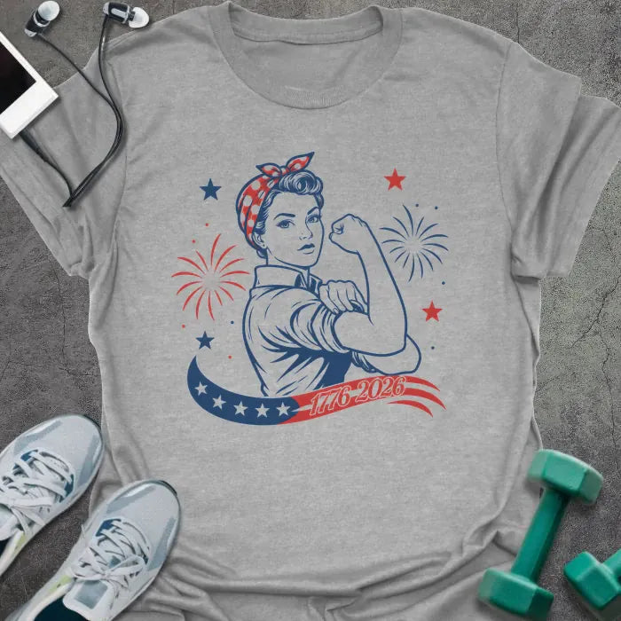 Sport grey t-shirt printed with "1776-2026" in navy, red, with Rosie the Riveter flexing her bicep among fireworks and stars