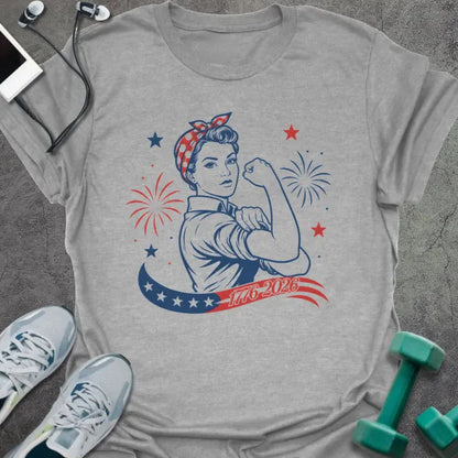 Sport grey t-shirt printed with "1776-2026" in navy, red, with Rosie the Riveter flexing her bicep among fireworks and stars