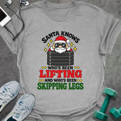 Sport grey t-shirt printed with "SANTA KNOWS WHO'S BEEN LIFTING AND WHO'S BEEN SKIPPING LEGS" in black, red and green, with Santa peering through binoculars over a stack of weight plates