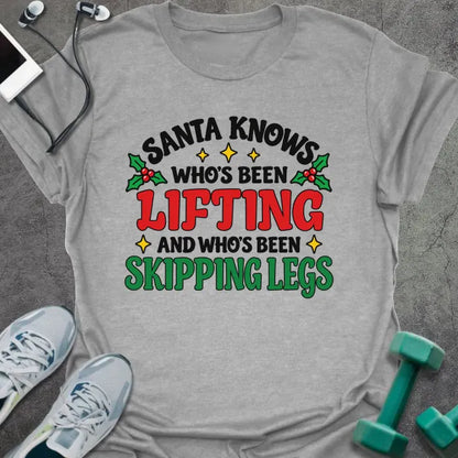 Sport grey t-shirt printed with "SANTA KNOWS WHO'S BEEN LIFTING AND WHO'S BEEN SKIPPING LEGS" in black, red and green, with holly and gold stars