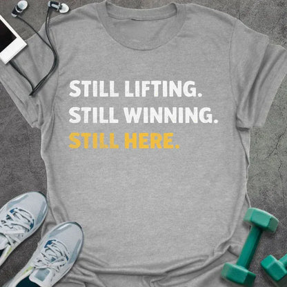 Sport grey t-shirt printed with "Still Lifting. Still Winning. Still Here." in white and yellow