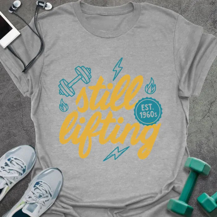 Sport grey t-shirt printed with "still lifting EST. 1960s" in yellow and cyan, with lightning bolts and dumbbell graphics