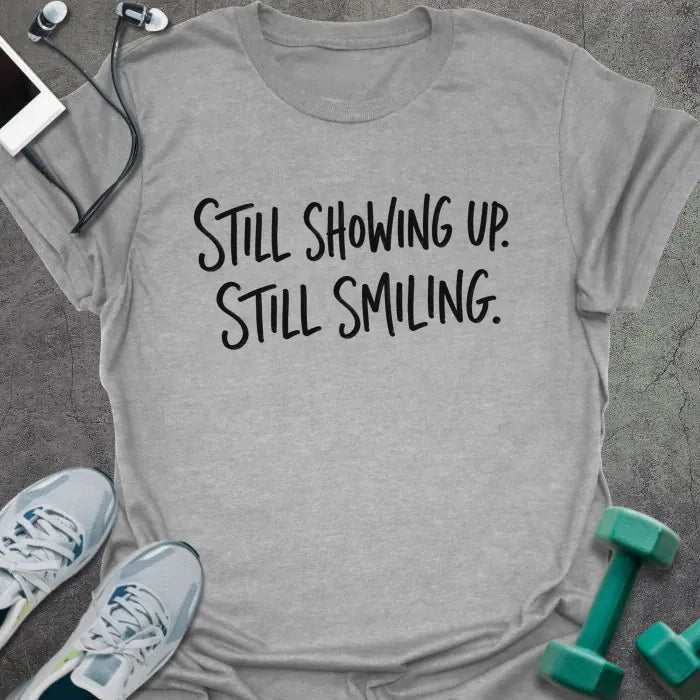 Sport Grey t-shirt printed with "STILL SHOWING UP. STILL SMILING." in black handwritten lettering