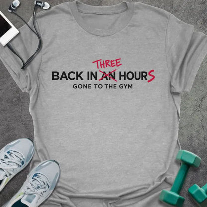 Sport grey t-shirt printed with "BACK IN AN HOUR, GONE TO THE GYM" in black, with "AN" crossed out and "THREE" and an extra S added in red to read back in three hours