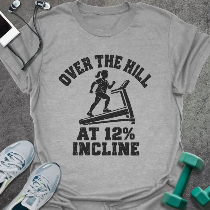 Sport grey t-shirt printed with "OVER THE HILL AT 12% INCLINE" in charcoal, with a woman walking on a treadmill